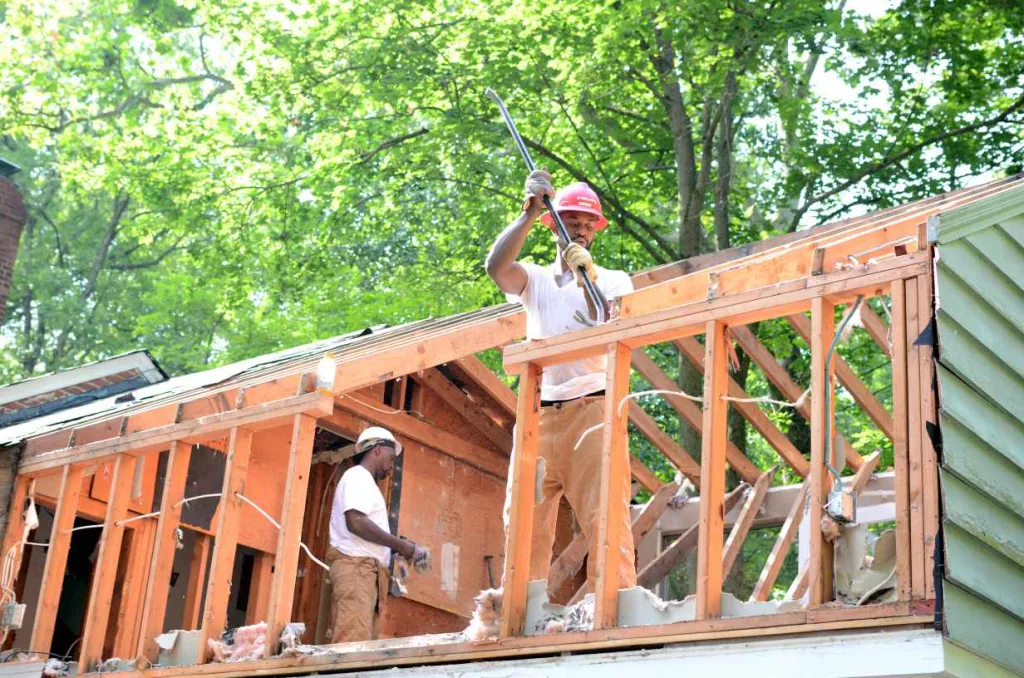 Two skilled workers salvaging valuable reclaimed wood and used building materials from a residential deconstruction project, contributing to the Baltimore non-profit Second Chance for sustainable home improvement.