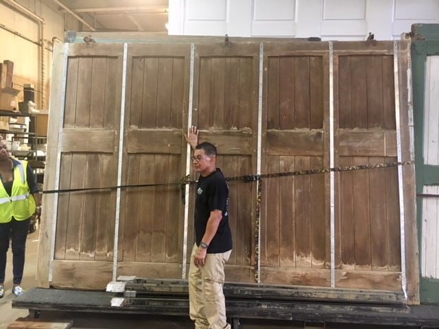 Warehouse staff with a set of five tall salvaged reclaimed wood panel doors, available as unique used building materials from Second Chance, a Baltimore non-profit.