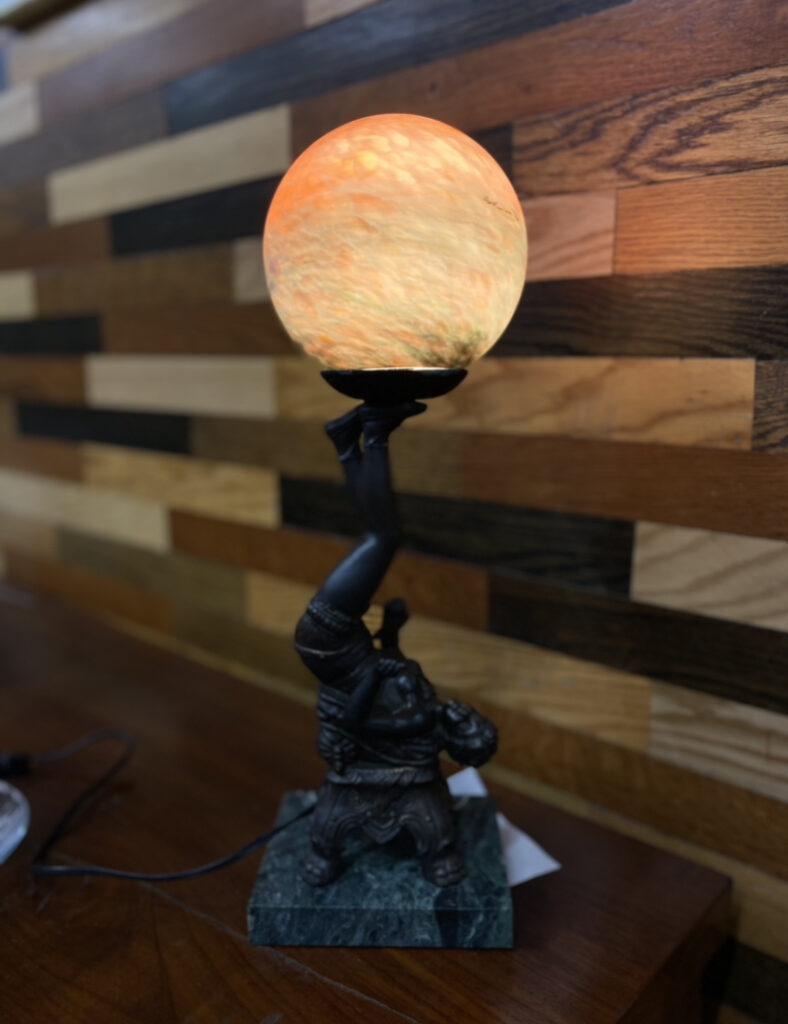 Vintage table lamp with glowing orange art glass globe and bronze figure on green marble base, offered by our Baltimore non-profit. Find unique secondhand lighting and decor for your home.